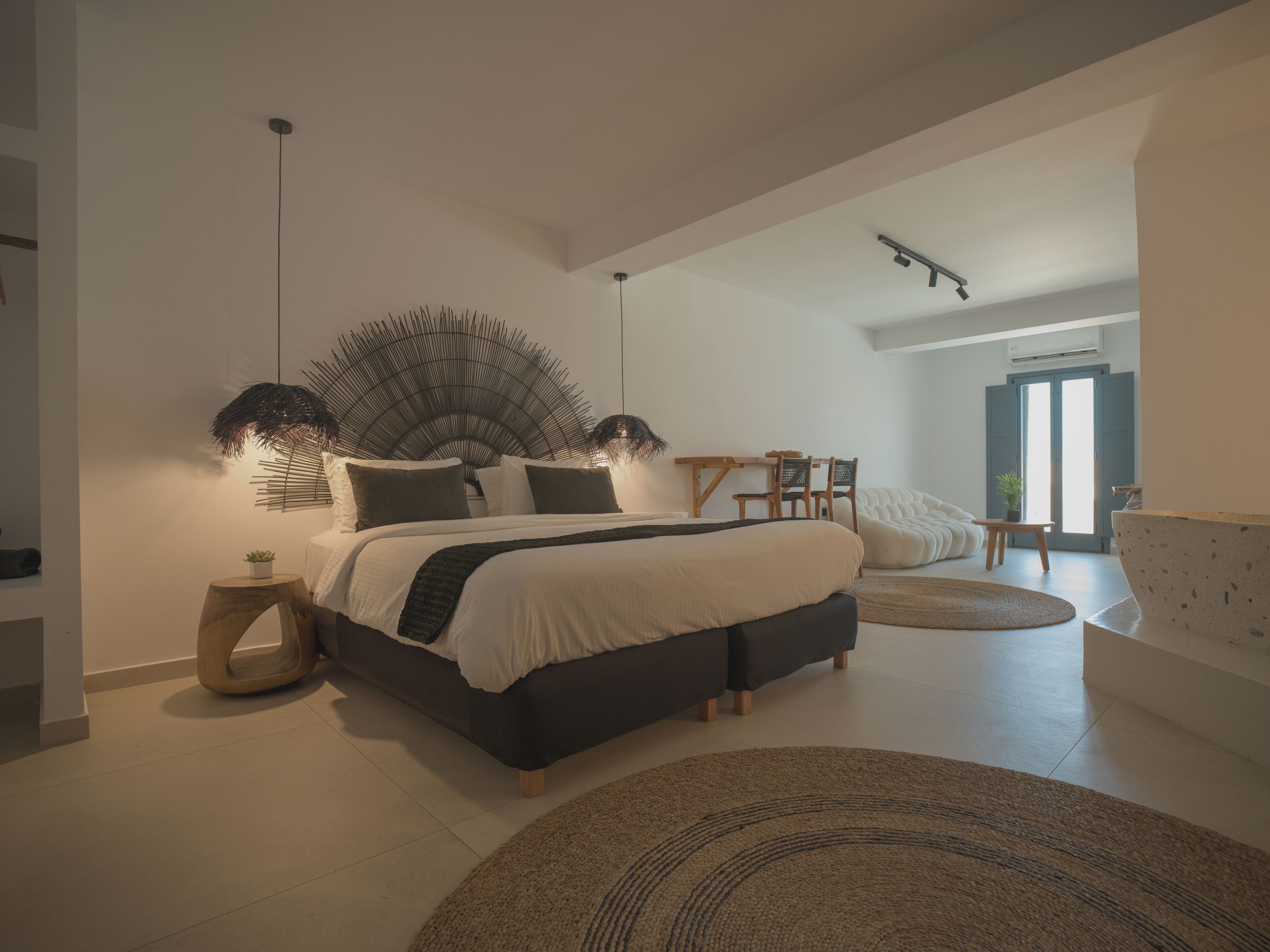 Ein modernes Schlafzimmer mit einem großen Bett, einem besonderen Deckenventilator und Blick ins Bad.