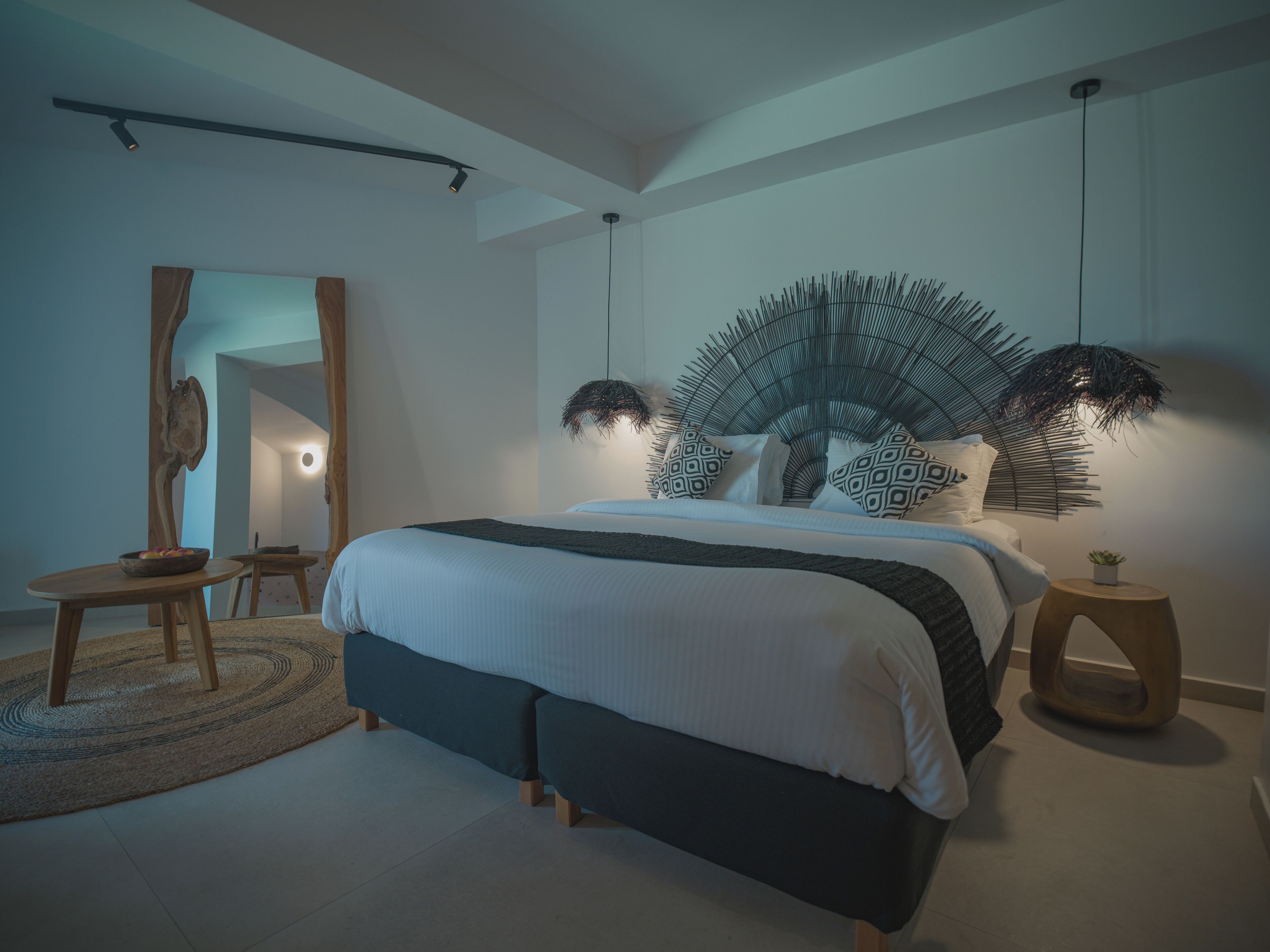 A modern bedroom with a large bed, a round wooden side table, a mirror, and a unique wall decoration.
