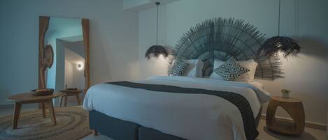 A modern bedroom with a large bed, a round wooden side table, a mirror, and a unique wall decoration.