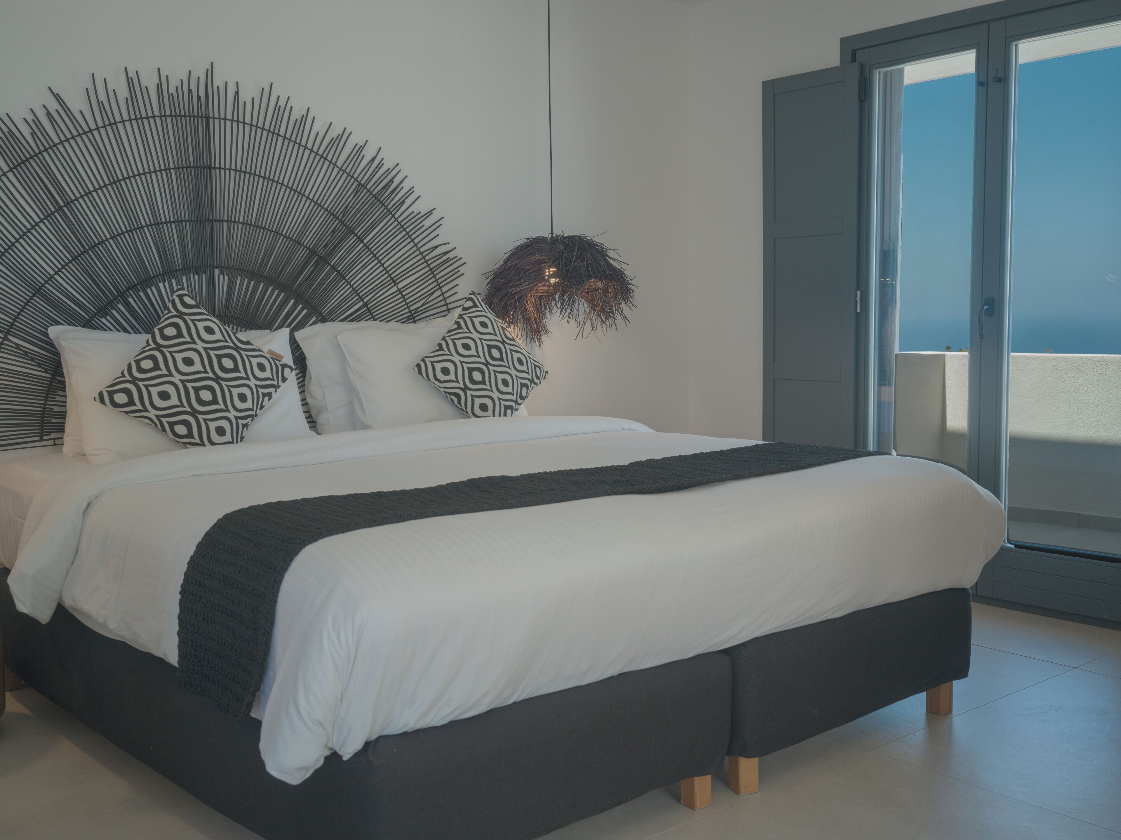 Een moderne slaapkamer met een bed, gekleurde kussens, een groot sierlijk hoofdeinde en uitzicht door een schuifdeur.