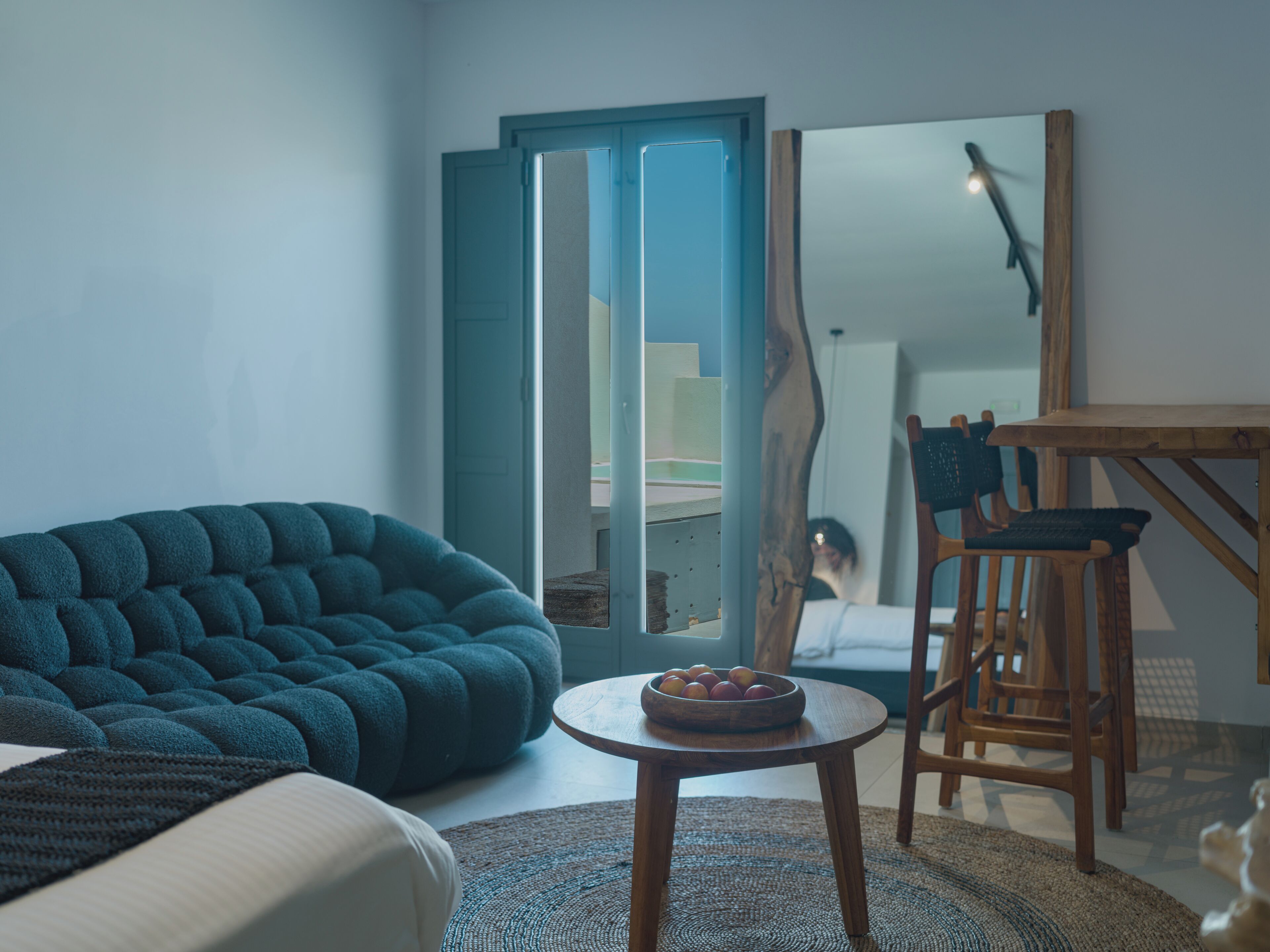 A modern living room with a sofa, a small round table with fruit, and a wooden chair.