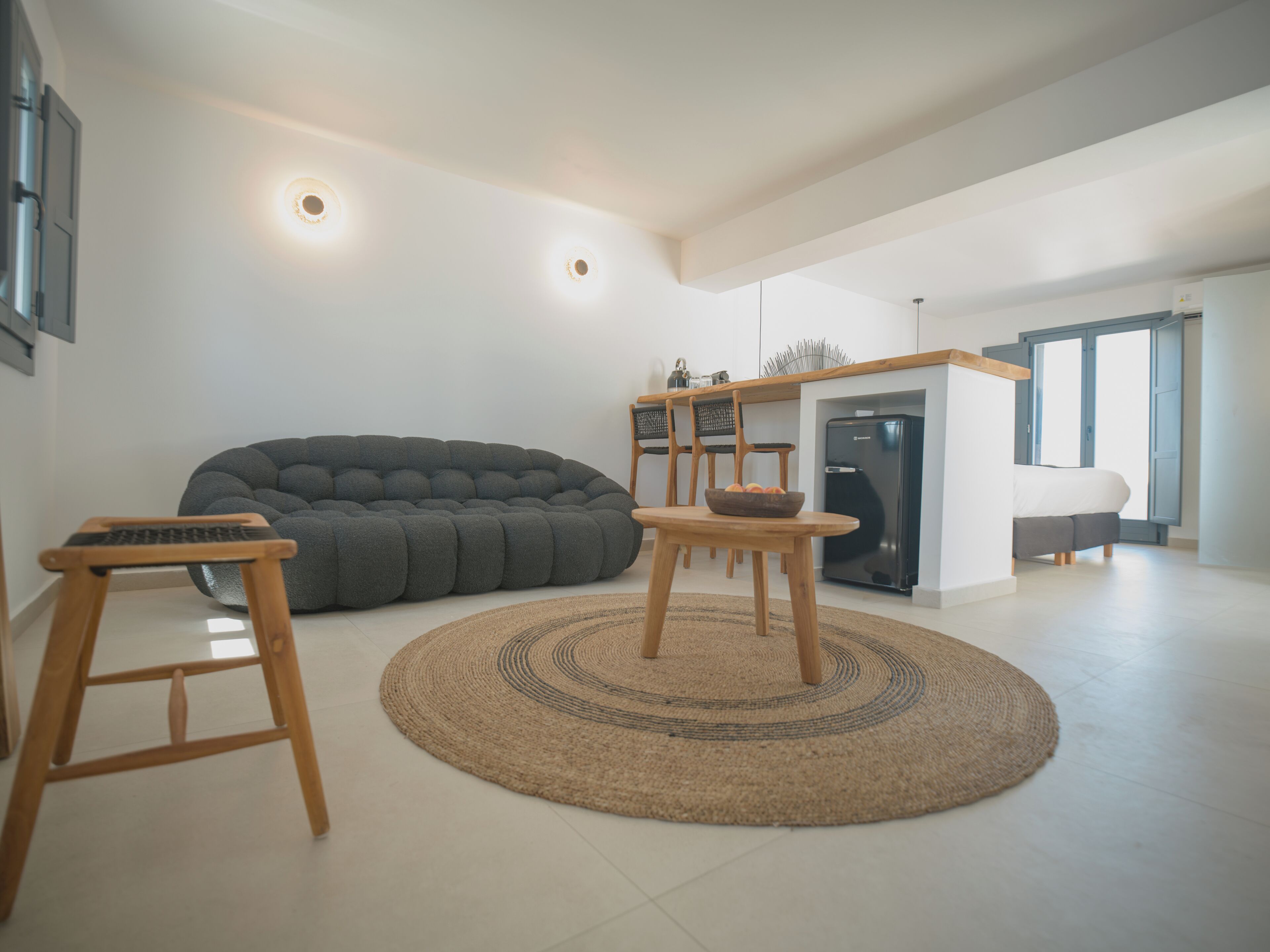 A modern living room with a large bean bag, a small wooden table, and a kitchen area with a refrigerator.