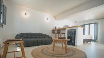 A modern living room with a large bean bag, a small wooden table, and a kitchen area with a refrigerator.