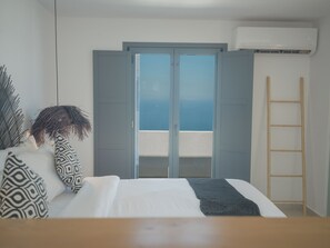 A bedroom with a bed, a view of the sea through a sliding door, a ladder, and an air conditioning unit. - Anemos Imerovigli Suites (Santorini)