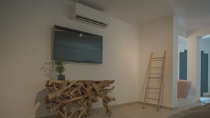 A modern living room with a large flat-screen TV mounted on the wall, a wooden console table, a potted plant, and a ladder leaning against the wall. - Anemos Imerovigli Suites (Santorini)