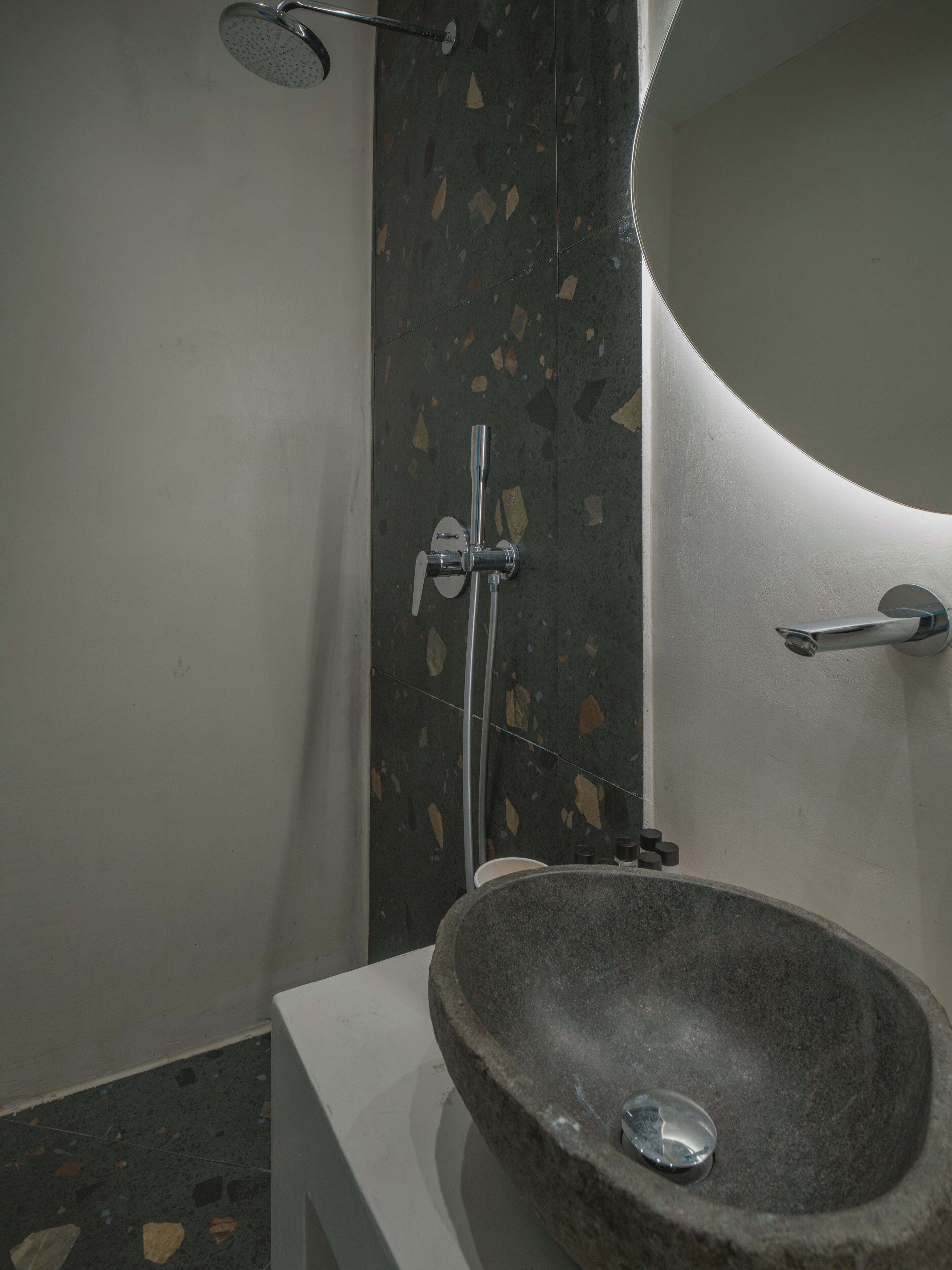 A bathroom with a stone sink, a shower, and a wall-mounted mirror.
