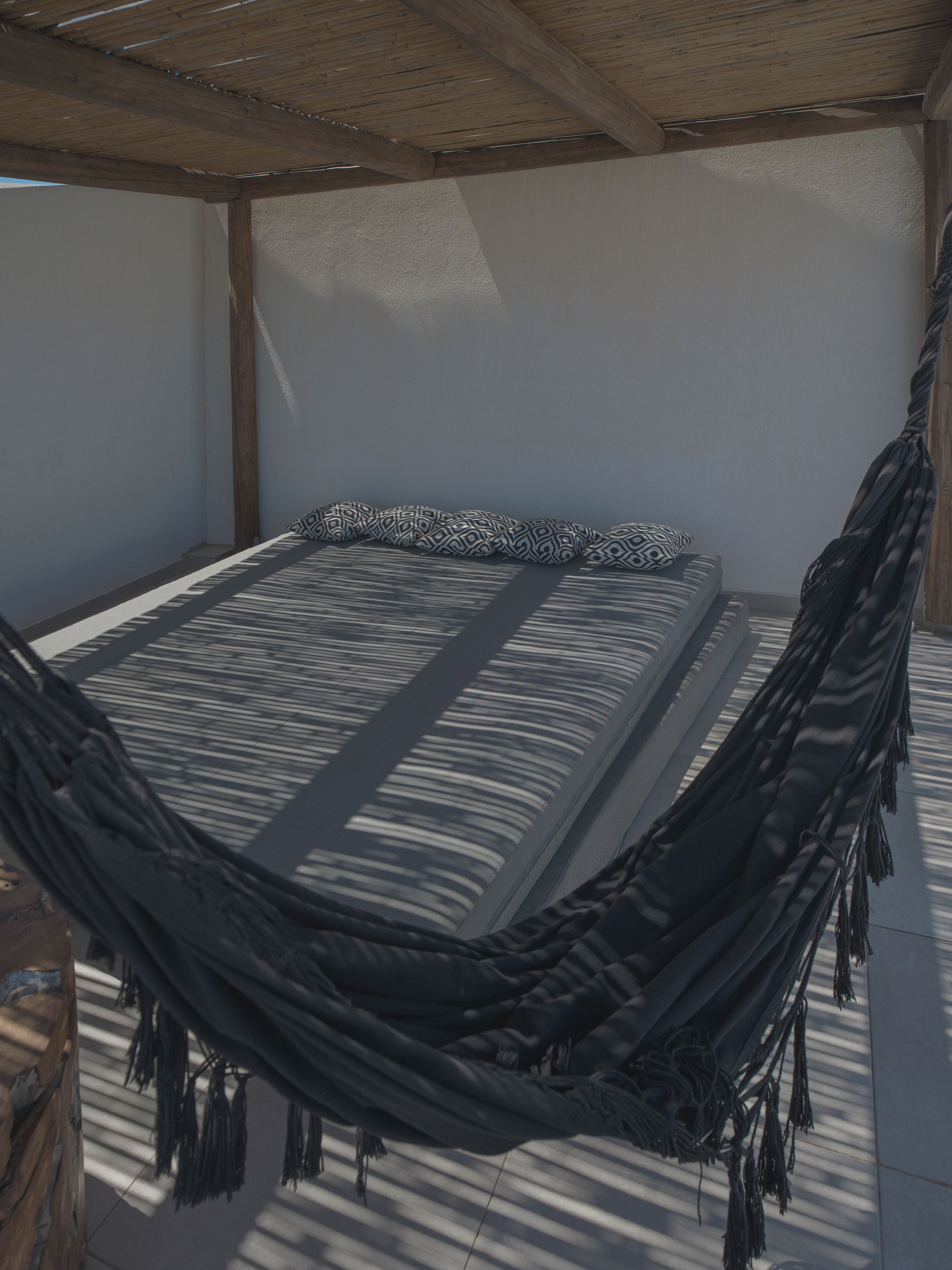 A hammock bed with a patterned pillow, wooden beams, and a tiled floor.