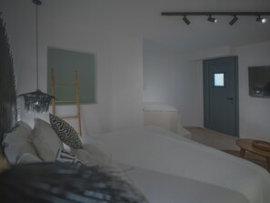 A bedroom with a bed, a bedside table, a lamp, a door, and a wall-mounted TV. - Anemos Imerovigli Suites (Santorini)