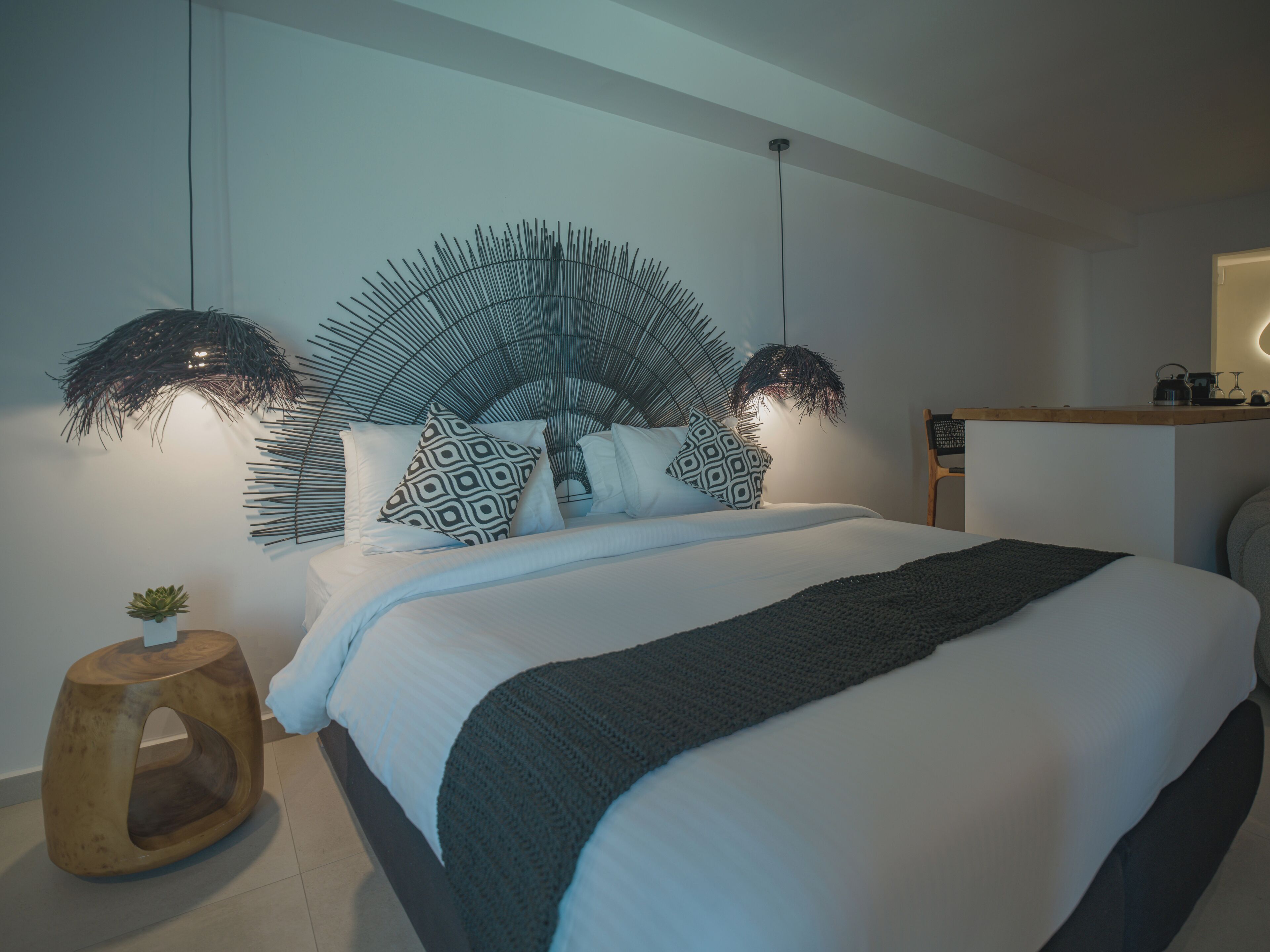 A modern bedroom with a large bed, patterned pillows, a wooden side table, and a wall-mounted light fixture.