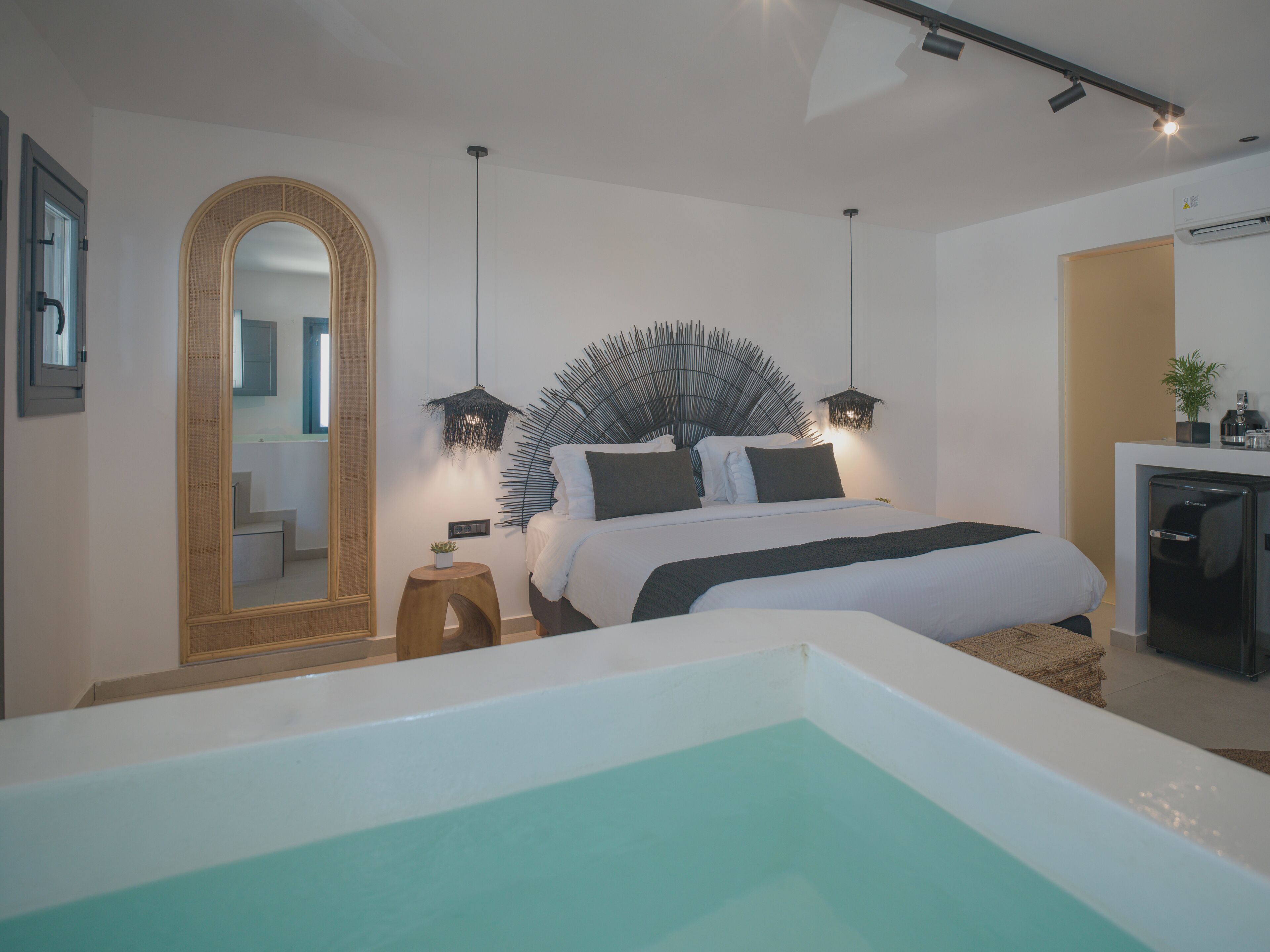 Un dormitorio moderno con una cama grande, una bañera integrada, un espejo y un pequeño escritorio con una planta.
