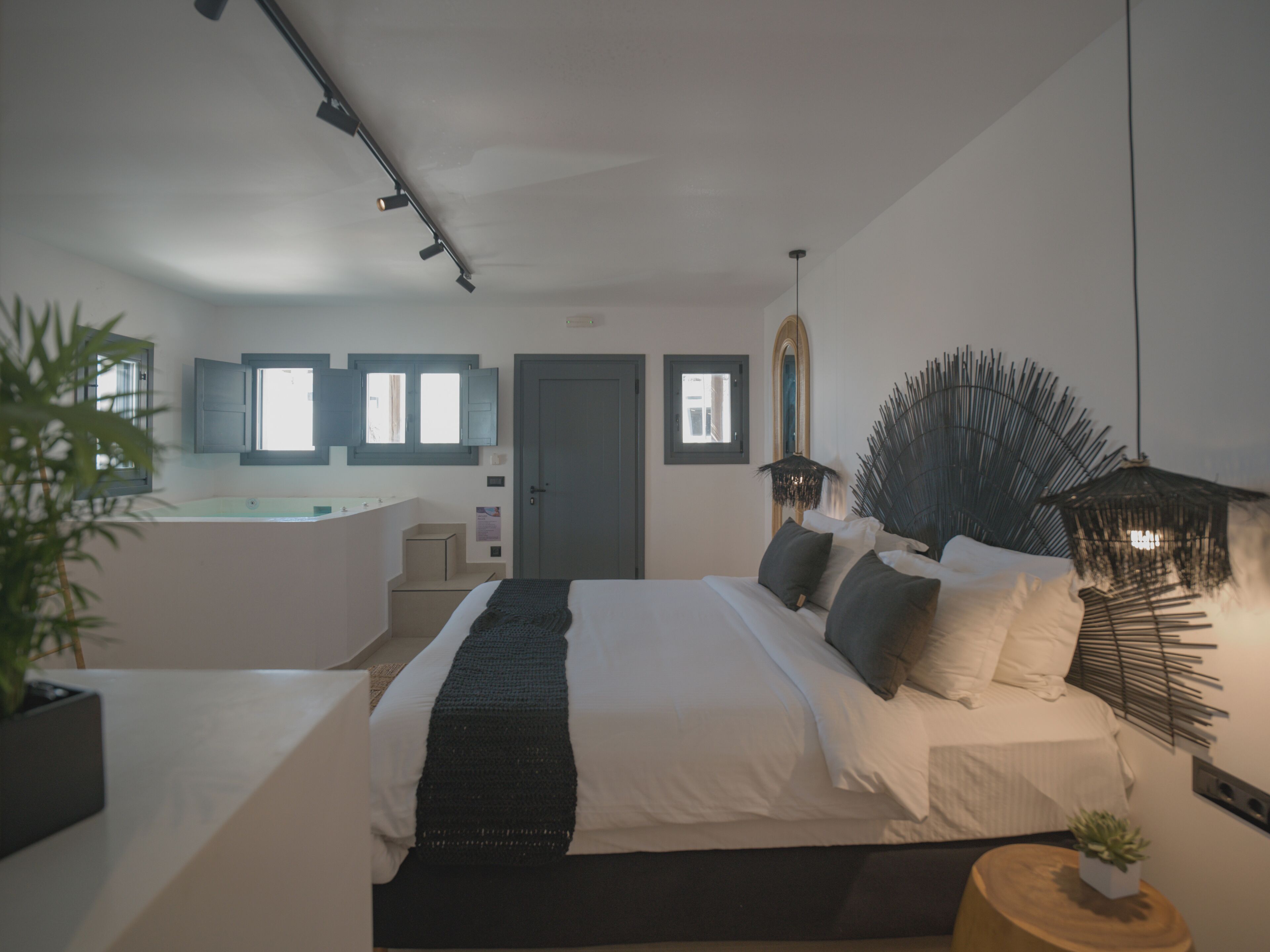 A modern bedroom with a large bed, bedside tables, a small desk, and a bathroom with a bathtub.