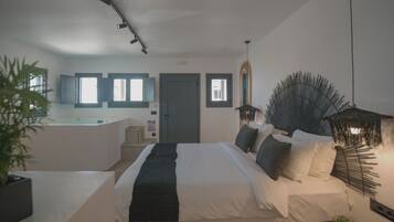 A modern bedroom with a large bed, bedside tables, a small desk, and a bathroom with a bathtub.