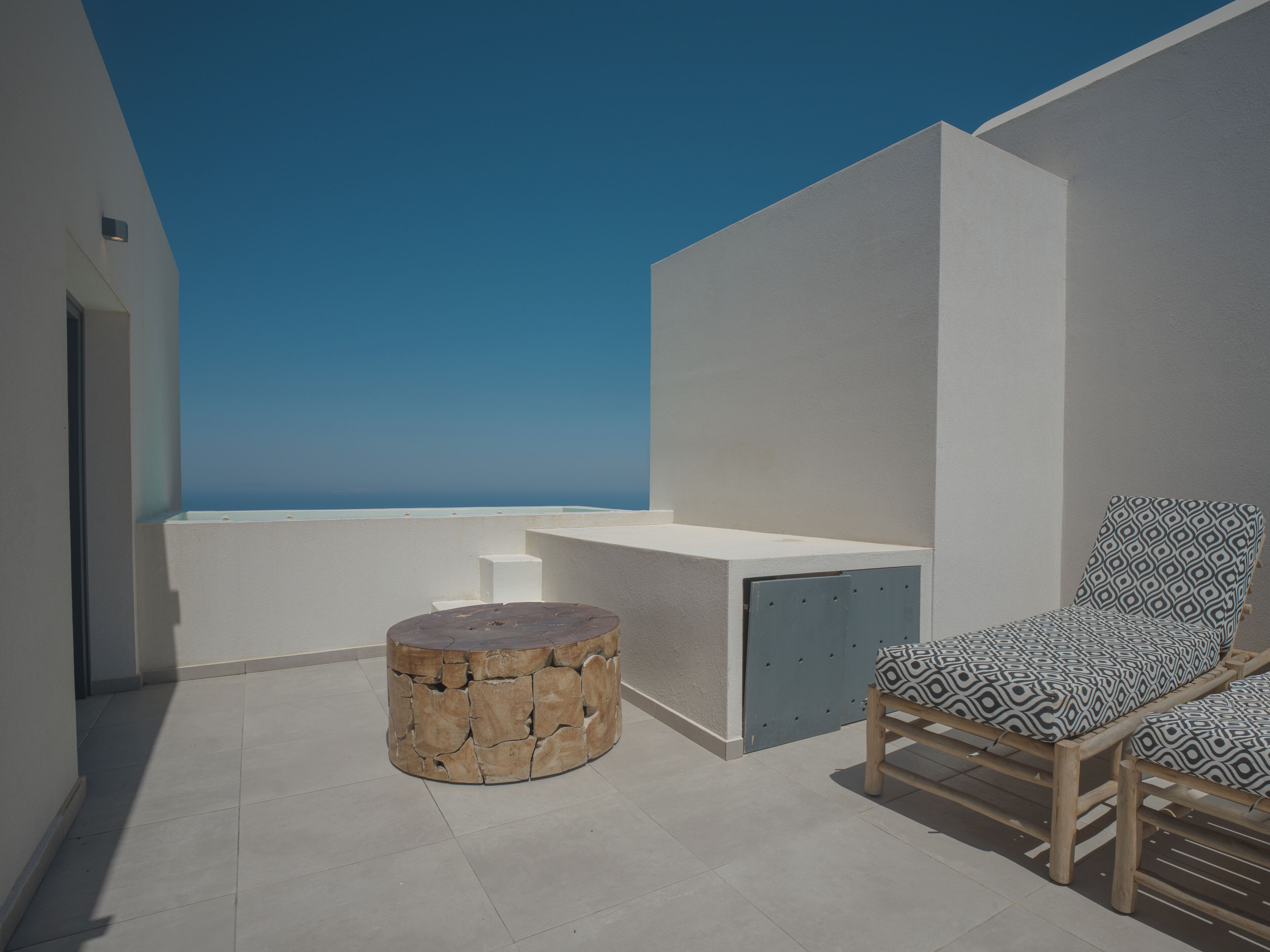 A modern outdoor seating area with a stone table and patterned chairs, overlooking a clear sky.