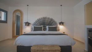 A modern bedroom with a large bed, two bedside lamps, a mirror, and a small plant. - Anemos Imerovigli Suites (Santorini)