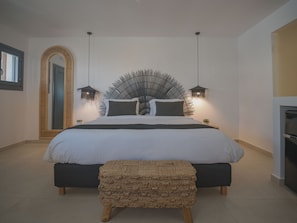 A modern bedroom with a large bed, two bedside lamps, a mirror, and a small plant. - Anemos Imerovigli Suites (Santorini)