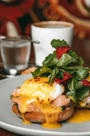 A breakfast dish with eggs, ham, and greens on a plate. - Anemos Imerovigli Suites (Santorini)