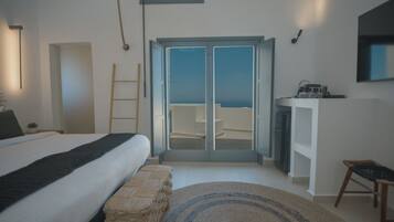 A bedroom with a bed, a bench, a desk, and a view of the sea through a sliding door.