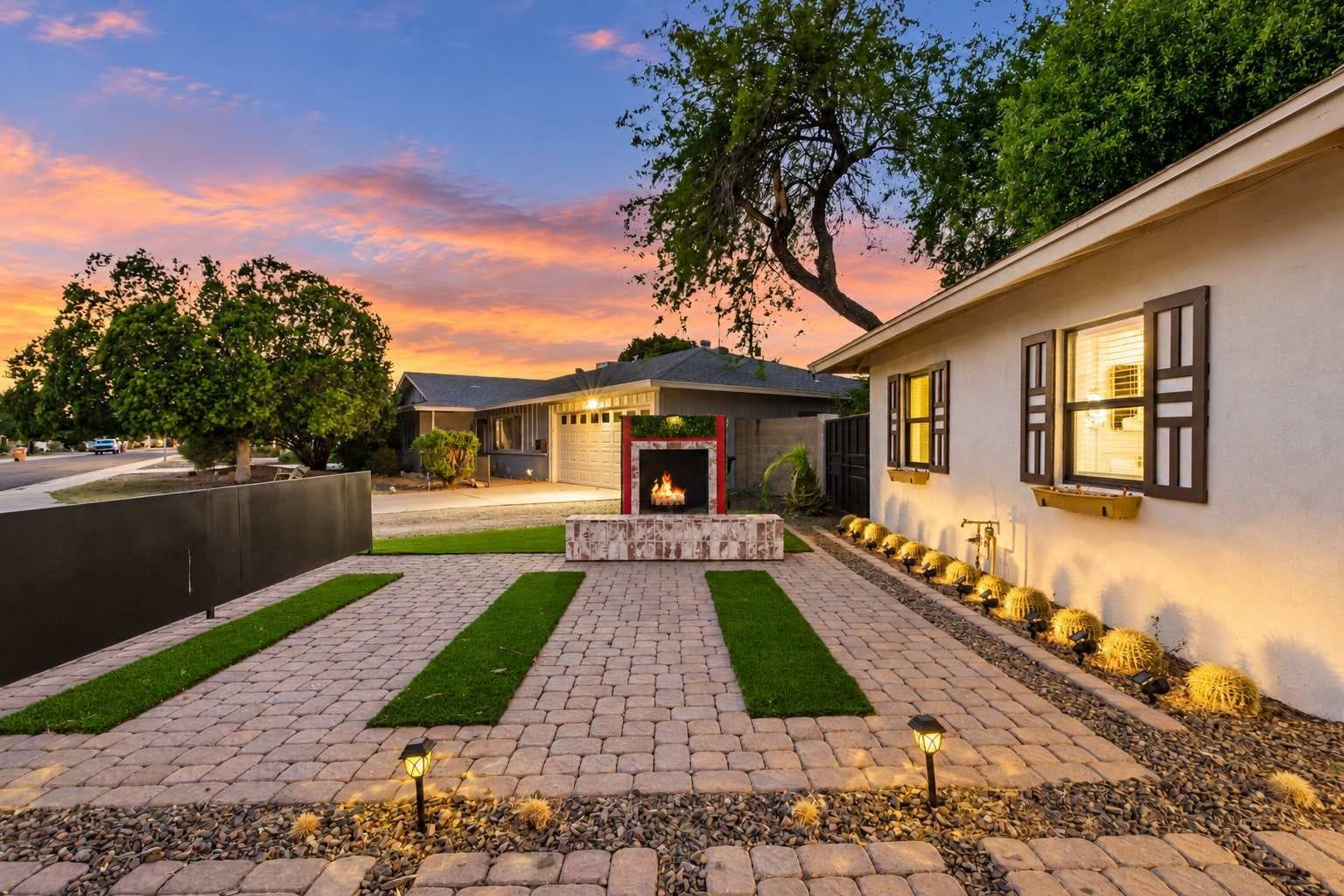A residential property with a paved driveway, a central fire feature, and a row of cacti along the side.