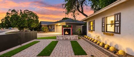 A residential property with a paved driveway, a central fire feature, and a row of cacti along the side.