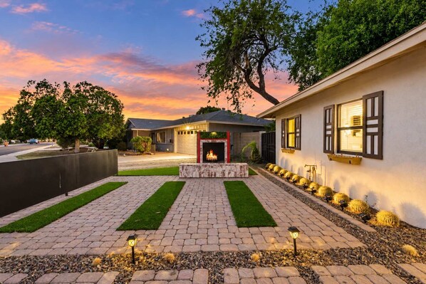 A residential property with a paved driveway, a central fire feature, and a row of cacti along the side.