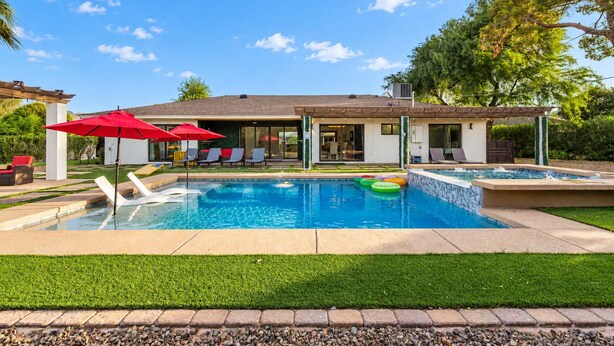 Une piscine résidentielle, agrémentée de chaises longues et de parasols, entourée d’une pelouse bien entretenue et d’une maison dotée d’une terrasse.