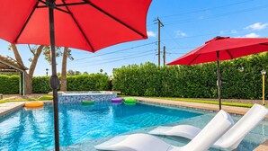 Une piscine équipée de chaises longues, de bouées gonflables et de parasols rouges.