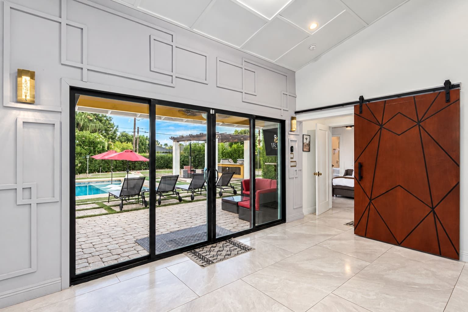 A modern interior with a sliding glass door leading to an outdoor patio area with lounge chairs and a pool.