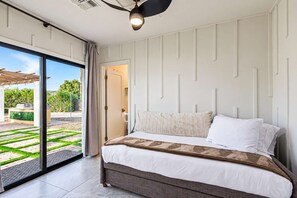 Ein Schlafzimmer mit Bett, Deckenventilator und Blick auf eine Terrasse mit Grill und Grünpflanzen.