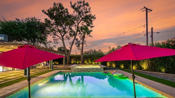 Piscina com dois guarda-sóis vermelhos, rodeada por árvores e um muro de pedra.