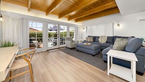 Una sala moderna con techo de madera, un sofá gris, una mesa de comedor con sillas y vistas al exterior a través de puertas de cristal.