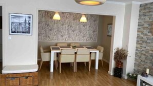 A dining area with a table and chairs, a hanging light fixture, and a cityscape picture on the wall.