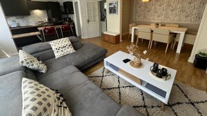 A modern living room with a grey sofa, a white coffee table, and a dining area with a white table and chairs.
