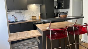 A compact kitchen with dark cabinets, a wooden countertop, a built-in stove, and red bar stools.