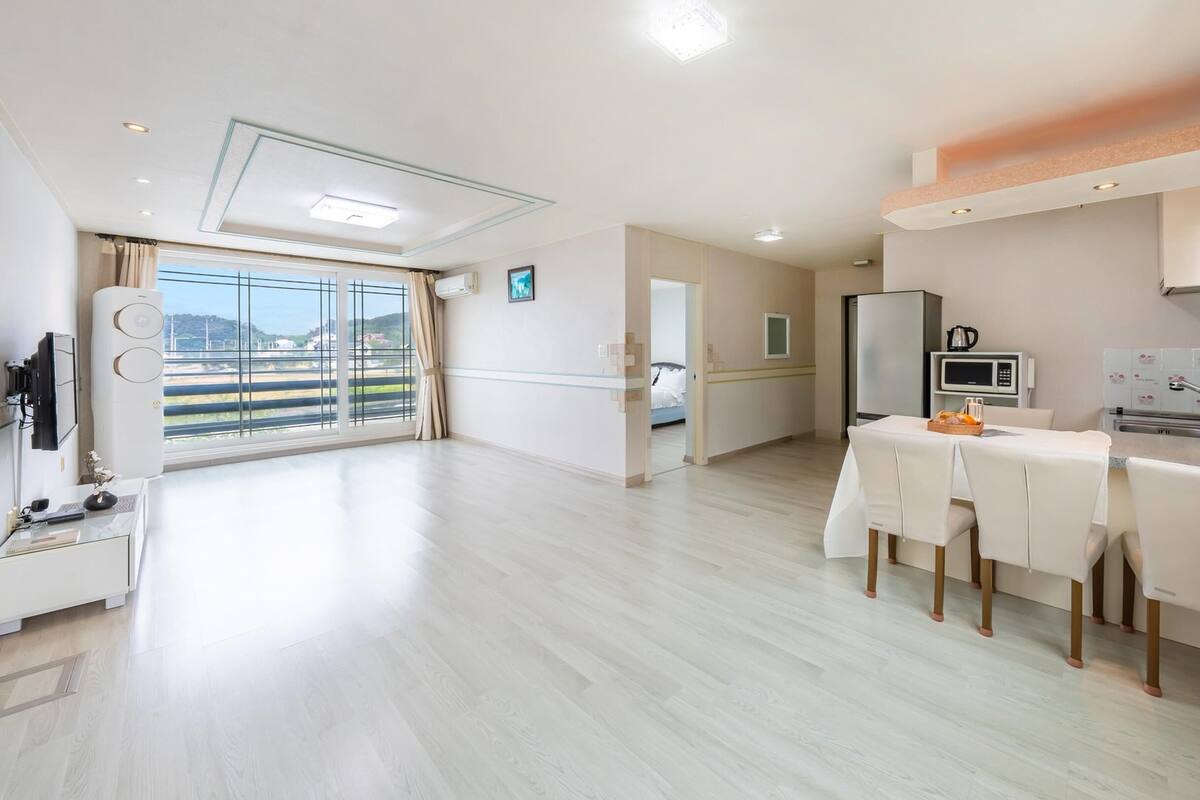 A spacious living area with a balcony, a dining area with a table and chairs, and a kitchenette.