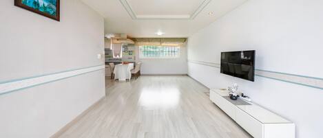 A modern hotel room with a dining area, a TV mounted on the wall, and a large window with a view of the outdoors.