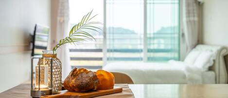 A table with a loaf of bread, a glass jar, and a candle in a modern room with a view of a building through large windows.