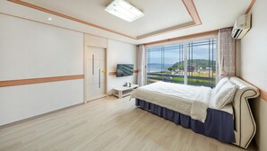 Ein Schlafzimmer mit Bett, Fernseher, Fenster mit Meerblick und Kleiderschrank.