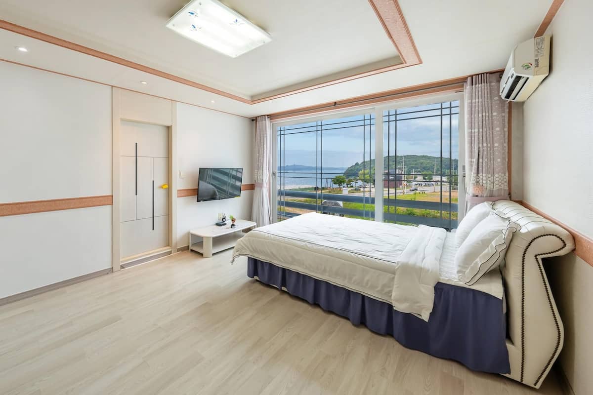 A bedroom with a bed, a TV, a window with a view of the sea, and a wardrobe.