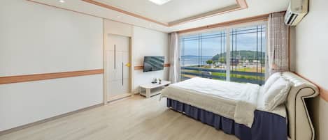 A bedroom with a bed, a TV, a window with a view of the sea, and a wardrobe.