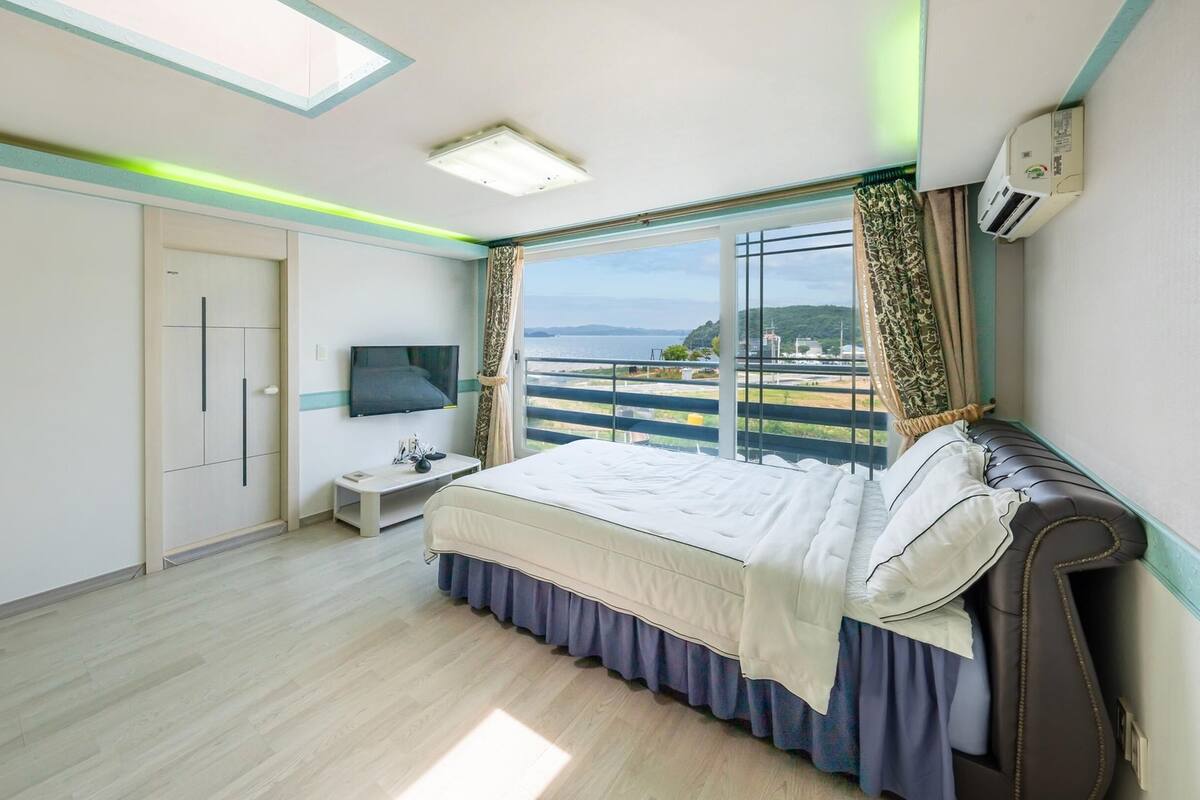A bedroom with a bed, a TV, a bedside table, a wardrobe, and a window with a view.