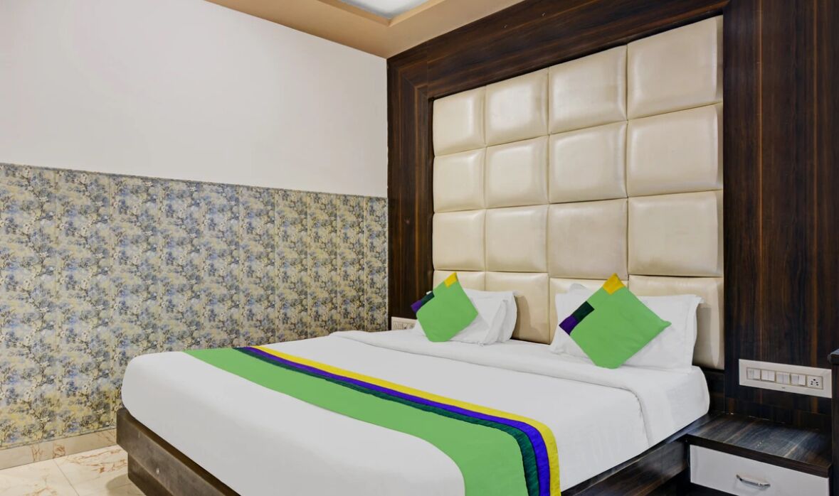 A hotel room with a large bed, floral wallpaper, a tufted headboard, and a nightstand with a drawer.