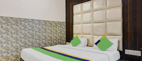 A hotel room with a large bed, floral wallpaper, a tufted headboard, and a nightstand with a drawer.
