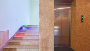 A marble staircase with colorful lighting, leading to an elevator with a digital display. - Mangal Residency (Udaipur)