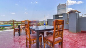 A rooftop terrace with a table and chairs, a water bottle, and a view of a cityscape and a water tower. - Mangal Residency (Udaipur)