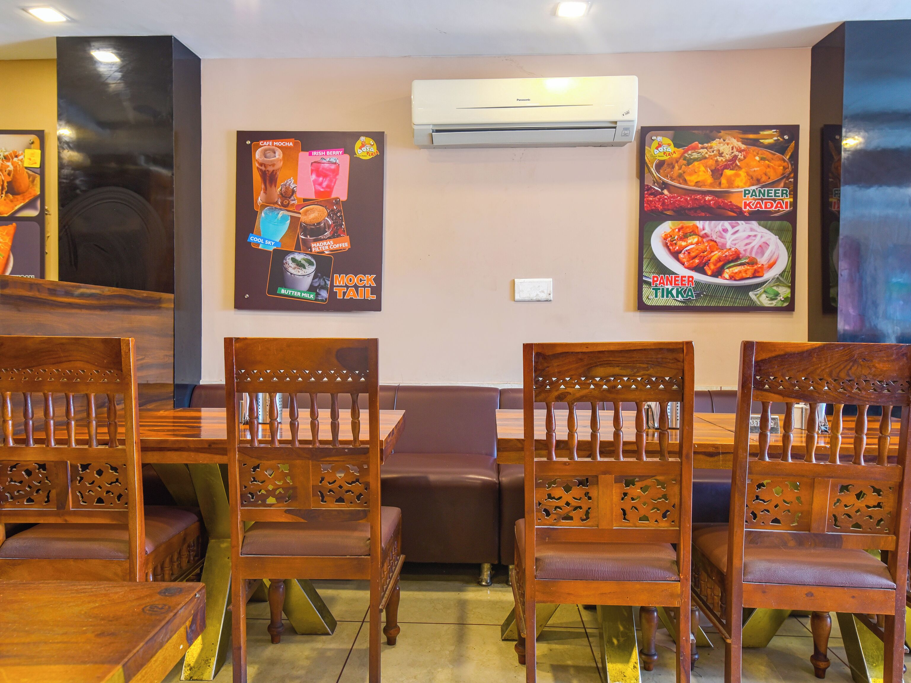 Interior de restaurant amb caires i taules de fusta, un aparell d'aire condicionat i cartells que anuncien plats del menú.