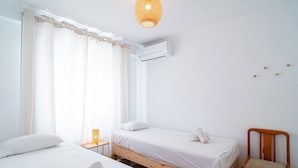 A room with two beds, a chair, a small table with a lamp, and an air conditioning unit. - Urban Comfort by Casasol (Nerja)