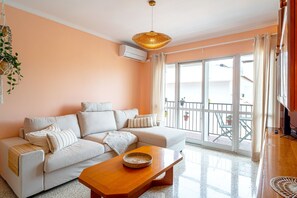 Una sala de estar con un sofá, una mesa de centro de madera y un ventanal con vistas a un balcón.