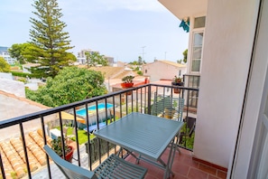 Ein Balkon mit einem Metalltisch und -stühlen, einem Blumentopf und Blick auf einen Swimmingpool und Grünflächen.