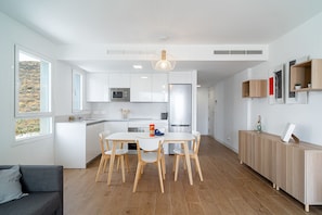 A modern kitchen with white cabinets, a central island, wooden chairs, and a built-in microwave.
