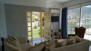 A living room with a sofa, a TV mounted on the wall, and a view of the outdoors through a glass door. - Villa Axia-Art 5pm from the sea (Evia)